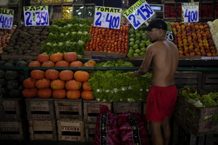 A shirtless man stands in front of a variety of vegetables.