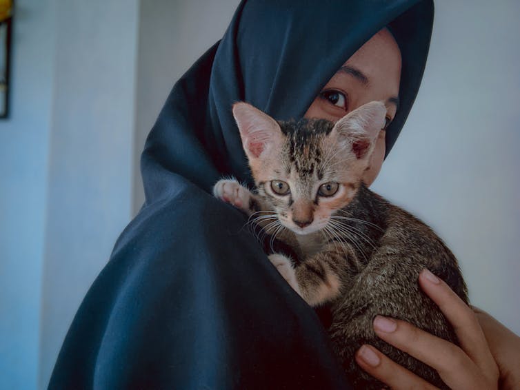 A woman holds a kitten on her shoulder.