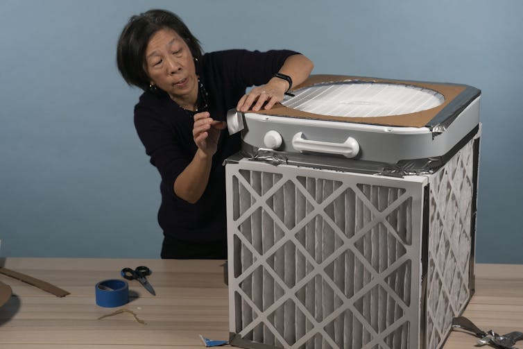 Woman tapes a box fan to a box of air filters.