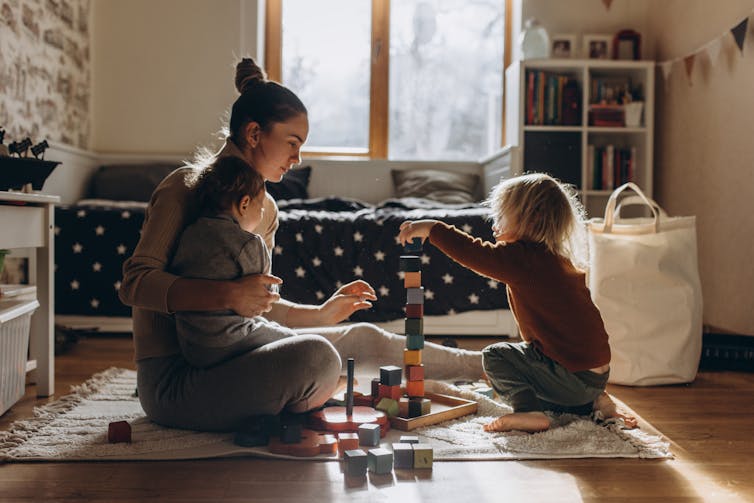 Mom sits on floor playing with wooden blocks with her children