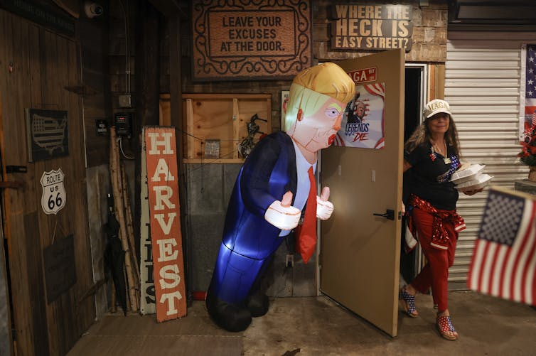 A woman walks out of a door that has a large blow-up balloon of Donald Trump.