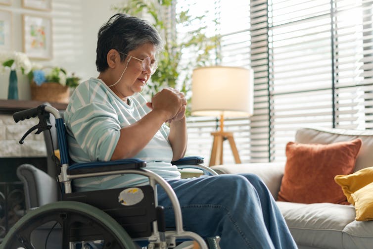 Older woman sits in a wheelchair in her lounge room.