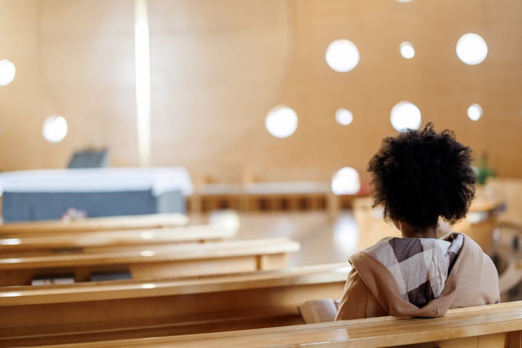 A woman with curly dark hair sits in a church pew, seen from behind.