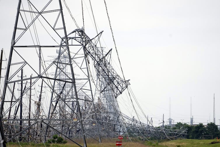 A line of transmission towers are folded over like a giant stepped on them. The wires are a tangled mess.