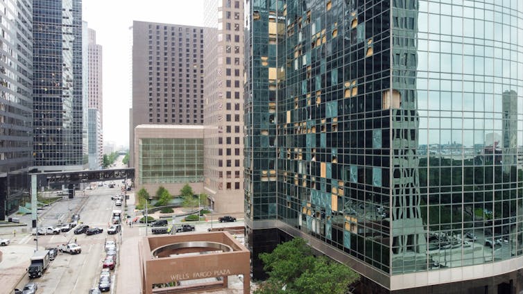 A view through downtown Houston shows windows blown out on one side of a building but not the other.