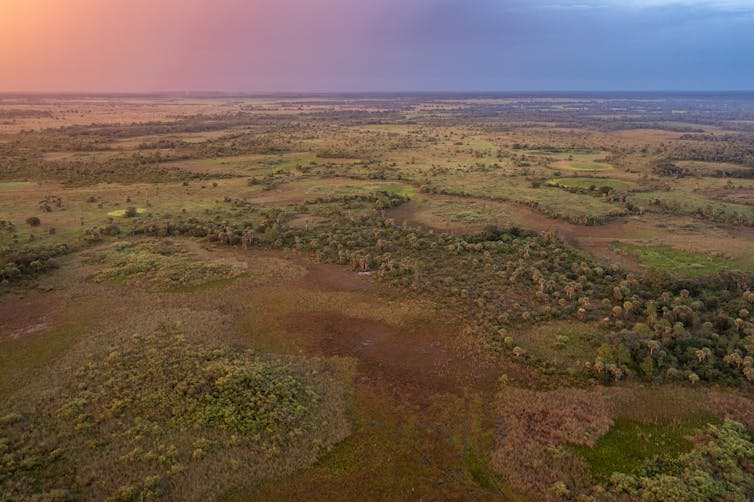 An orange, pink, purple and blue sky over large area of wetlands