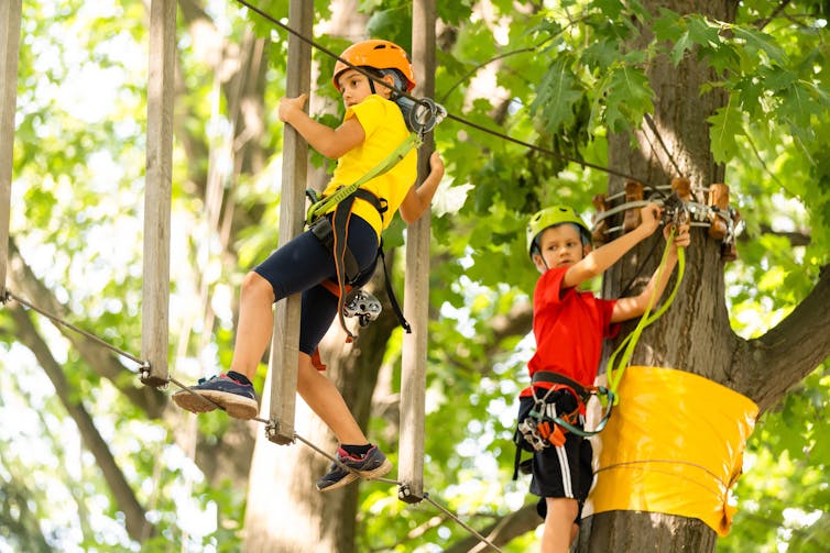 Two children climb on a ropes course.