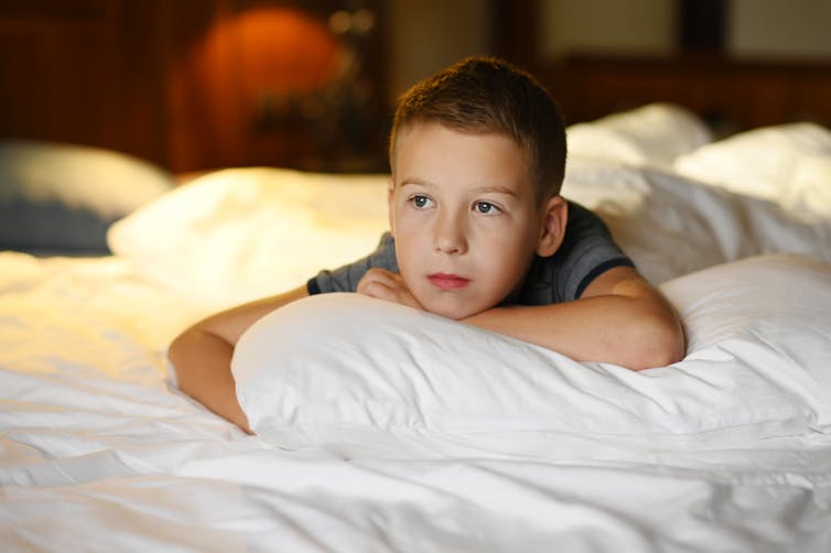 A young boy lies on a pillow on a bed.