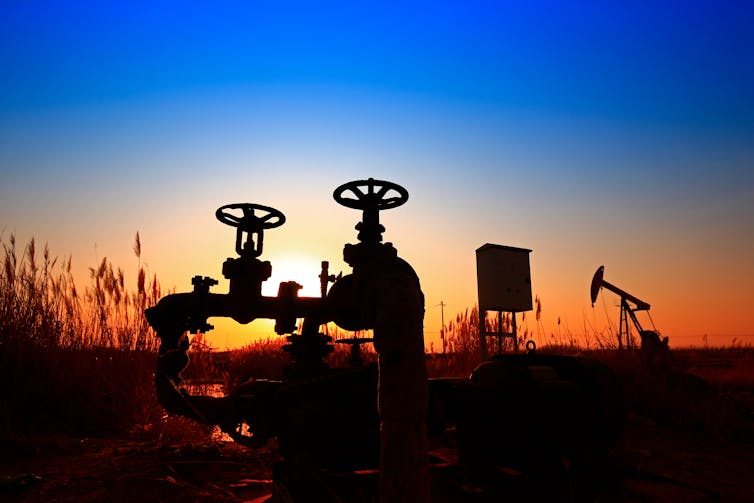 A valve and an oil derrick at dusk.
