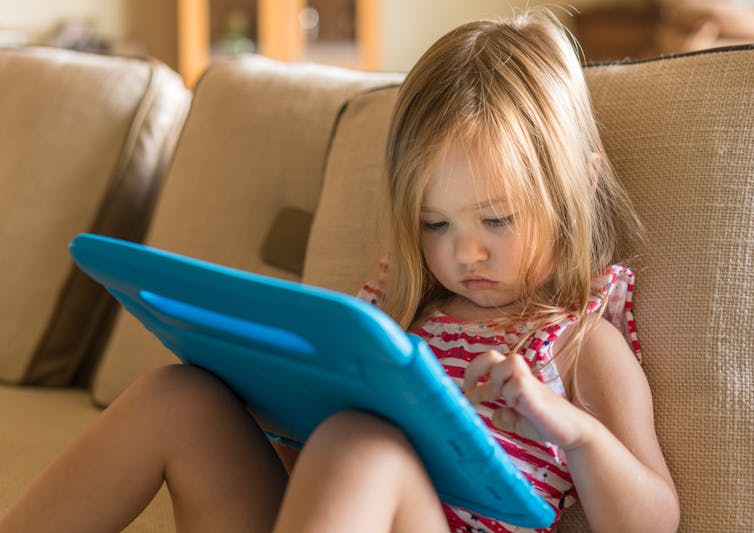 Toddler sitting on sofa, watching iPad