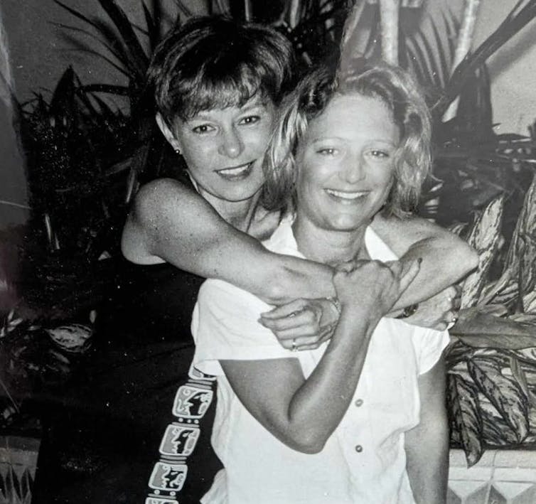 A young woman with her arms around the neck of another, both smiling