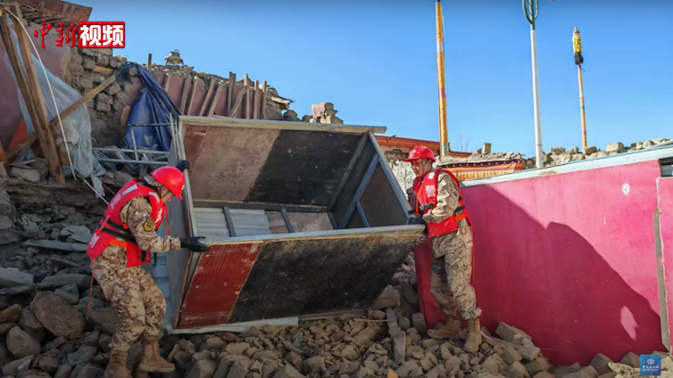 Two people move a container on a hill of rubble.