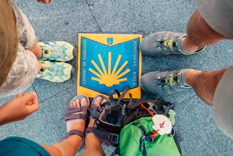 Three people standing around a Camino sign on the ground