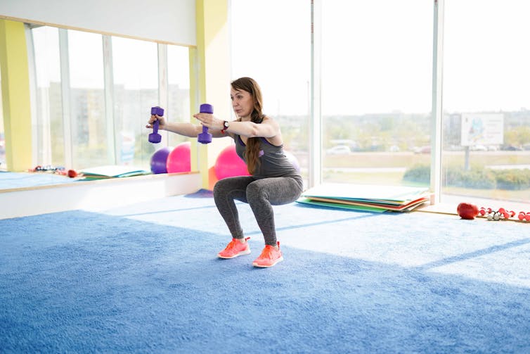 A middle-aged woman performs a squat using dummbells.