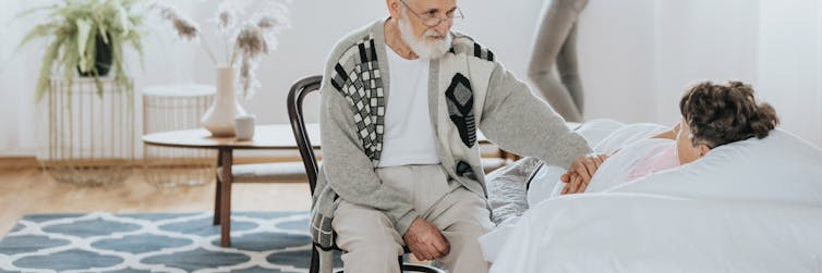 A man with gray hair sits by a woman's bedside