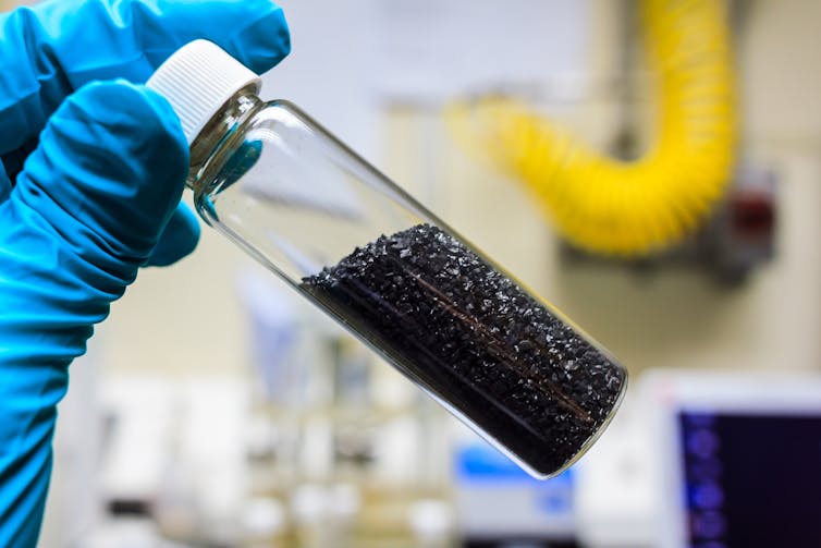 A vial of black carbon being held by a lab technician wearing a blue glove.