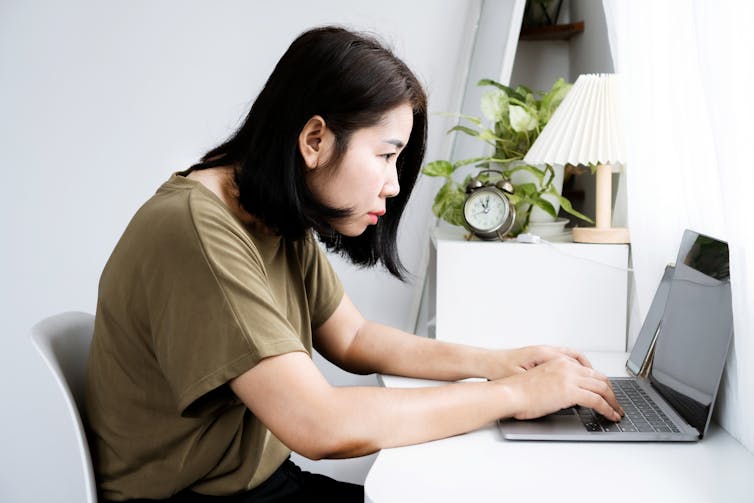 A woman sits hunched over her laptop