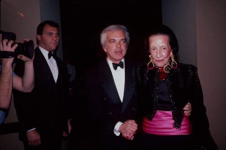 Elegantly dressed elderly woman is led by a youthful man wearing a tuxedo.