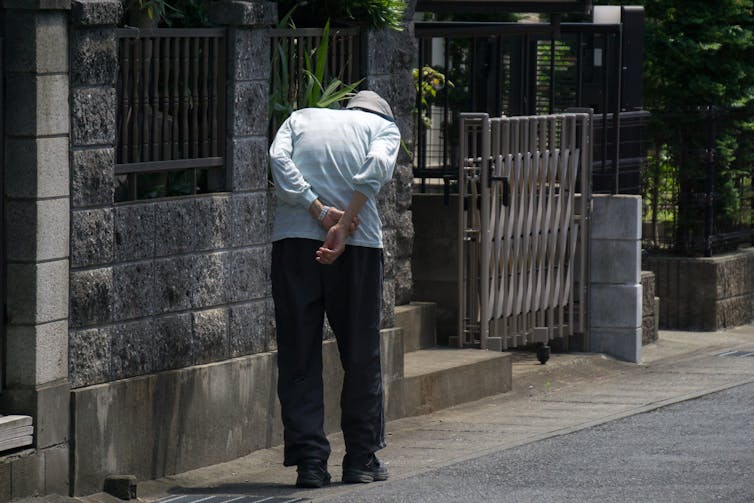An older man with a curved back walks on a path.