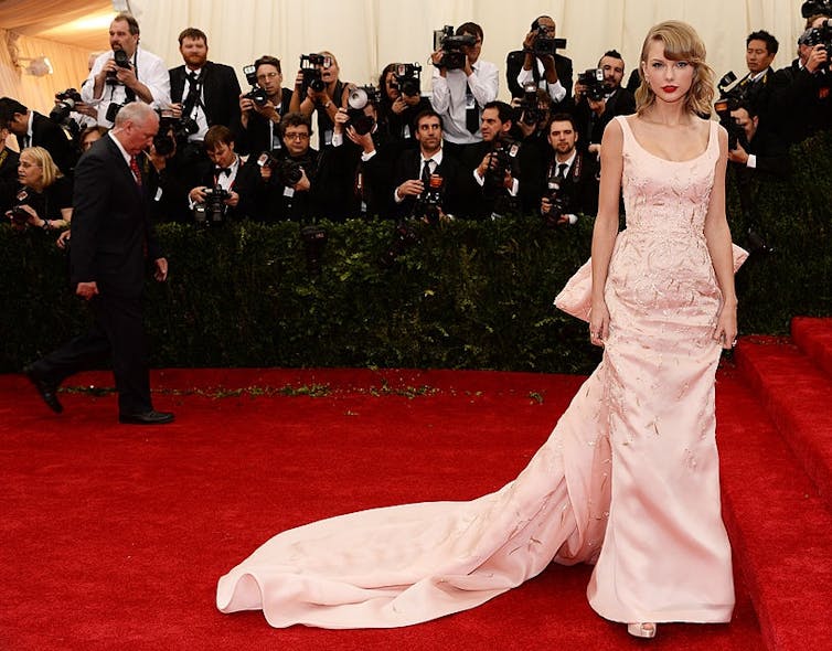 Young woman poses on red carpet in front of a hoard of photographs.