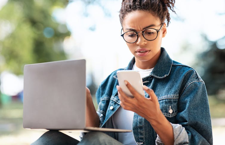 Young woman looking at phone and laptop