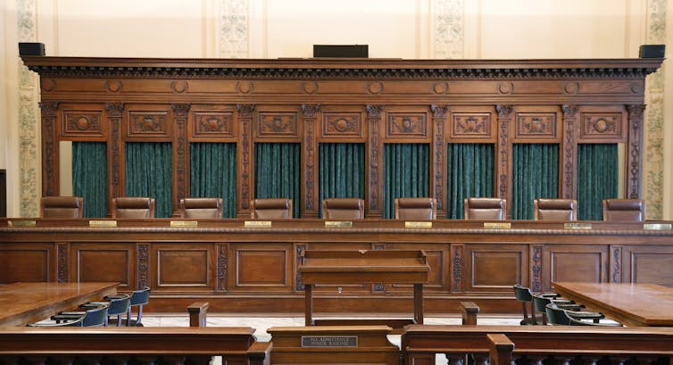 A large wooden dais with nine brown wooden seats behind its desk.