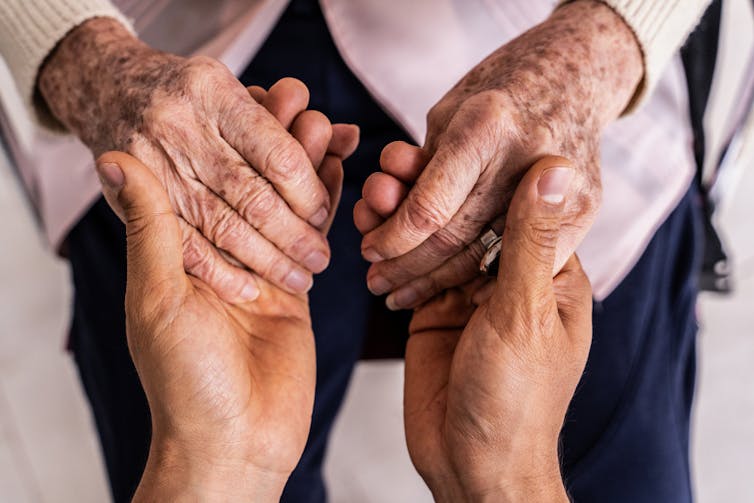 The hands of an older woman and a caregiver, clasped