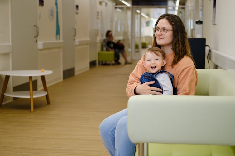 A mother sits with a toddler on her lap in a waiting area.