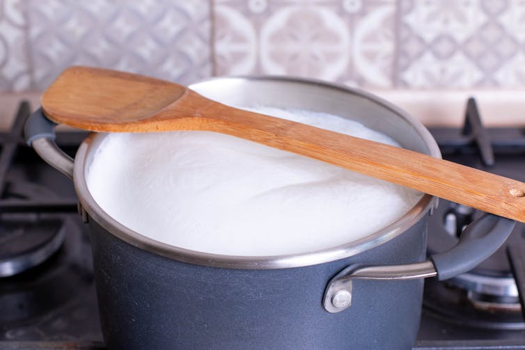 A pot of foamy milk on a stovetop with a wooden spoon placed across it.