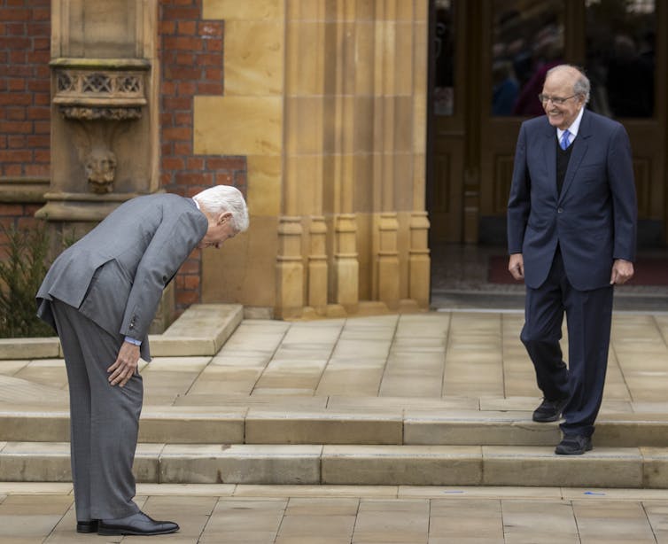 Two men in suits, one of them bowing to the other.