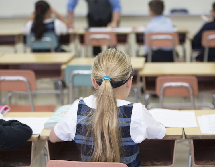 A rear view of a girl siting at her desk in class.