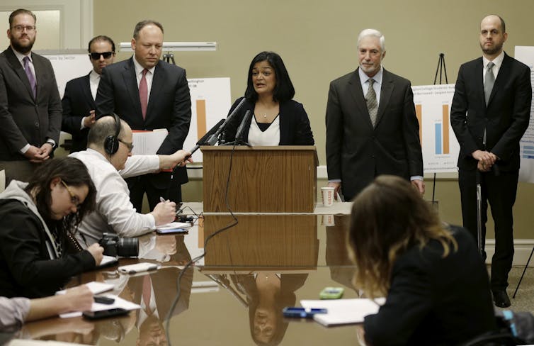Woman speaks at lectern while reporters take notes.