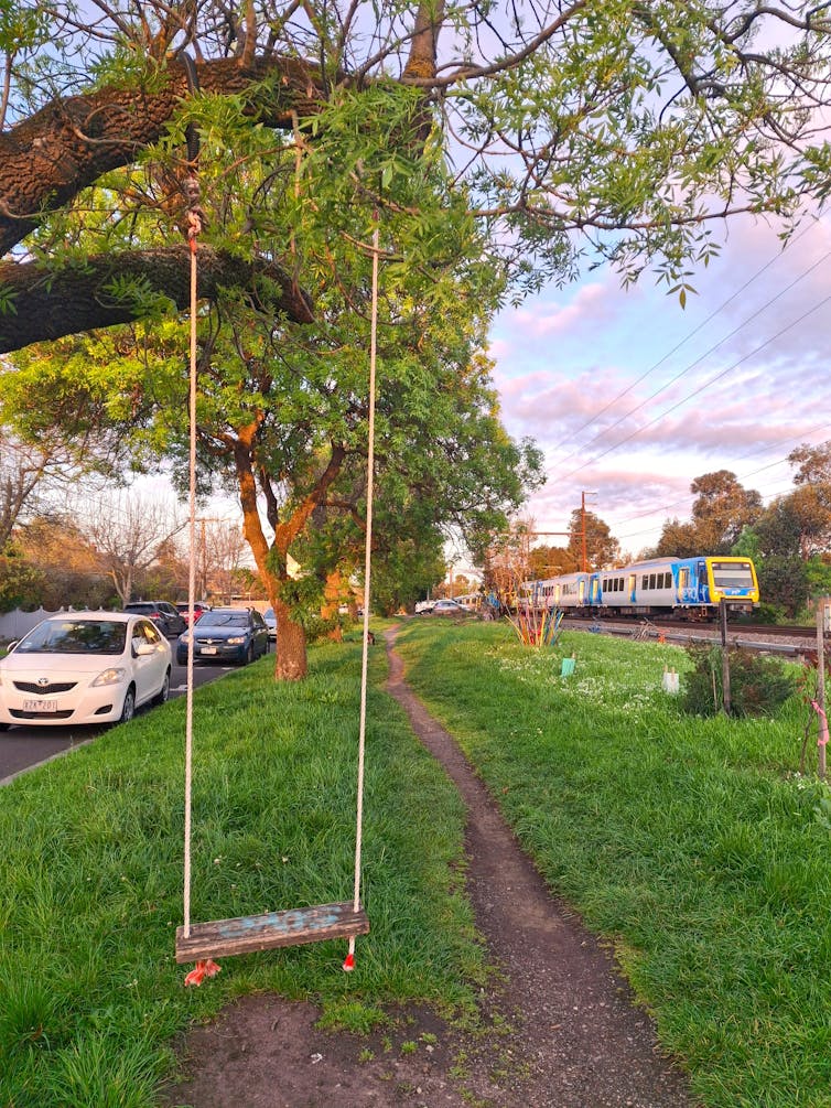 Informal green space between a road and rail line, with a swing hanging from a tree and art installation in the background.