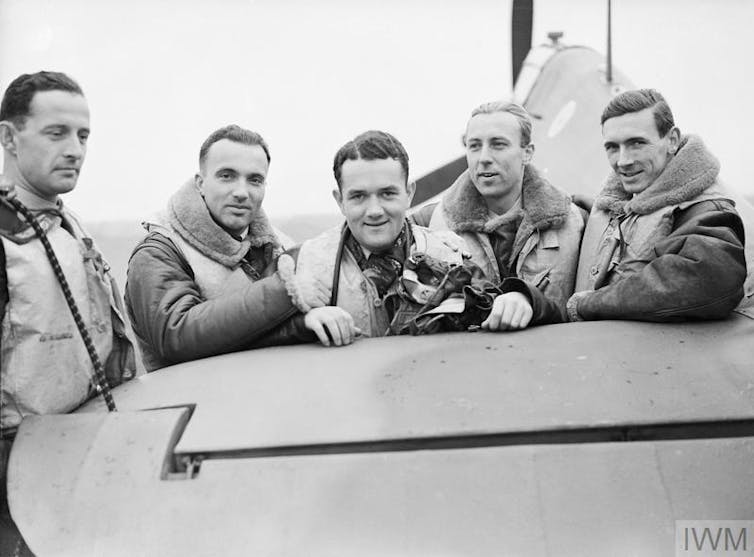 Young polish pilots smile as they pose for a photograph with a fighter aircraft during the second world war.