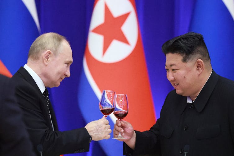 Two men in suits push wine glasses together.