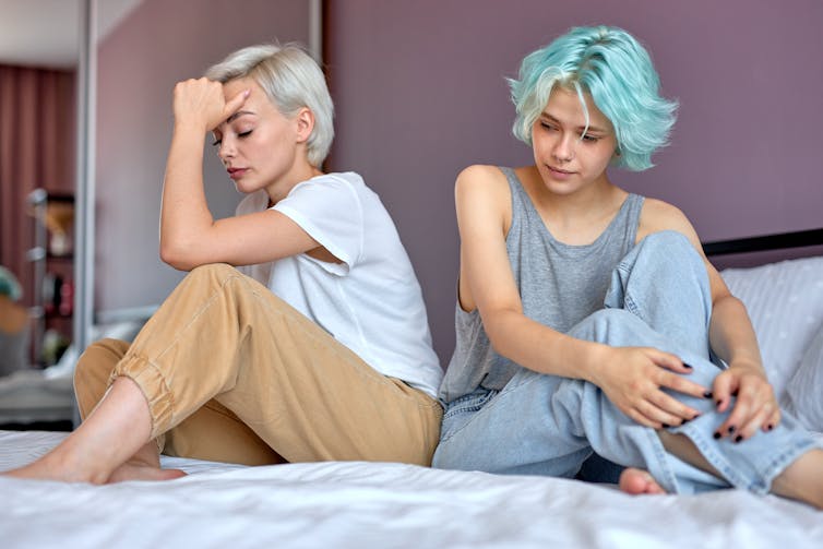 Two young women have a disagreement with each other while sitting on a bed.