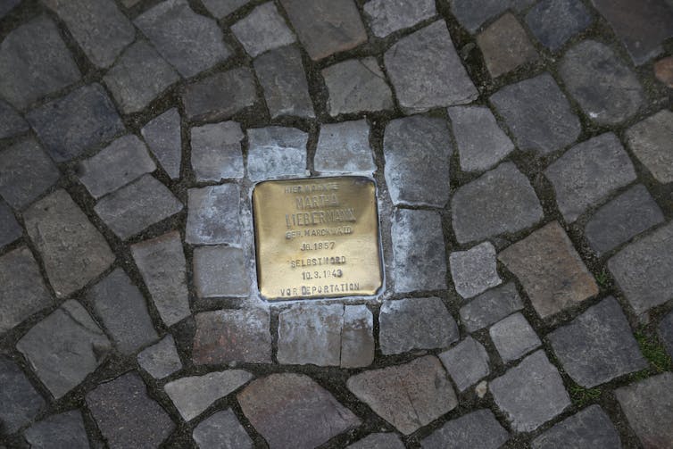 A gold stolperstein set into a cobbled street.