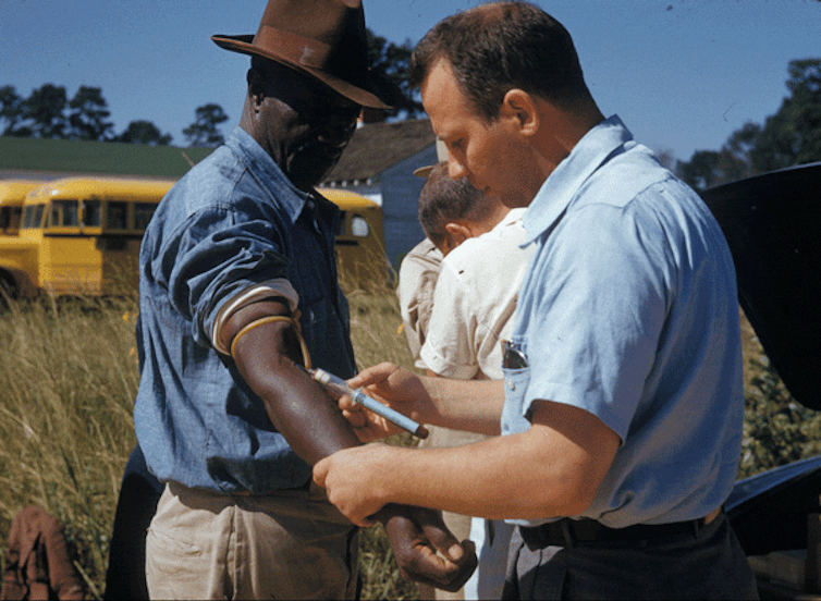White researcher injecting a Black participant in the Tuskegee Study with a syringe