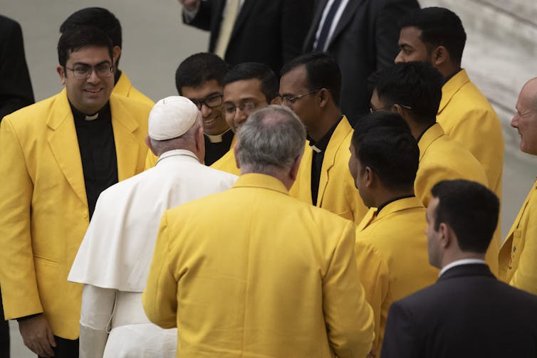 A man in white greets several people in yellow jackets.