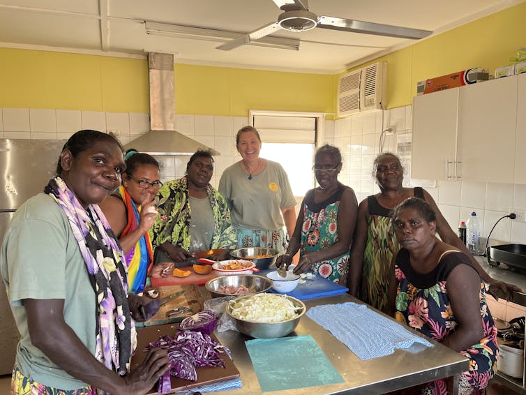 A group of people in a kitchen around a workbench with salads.