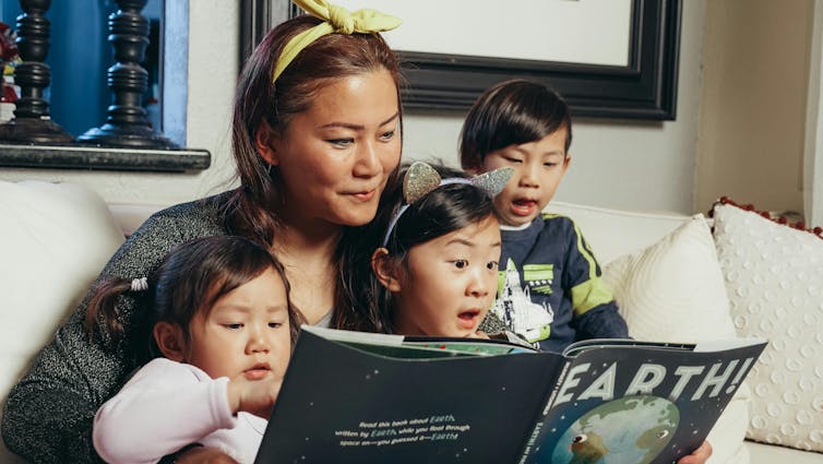 A woman reads a book about Earth to three small children.