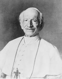 A half-length portrait of a man in white priestly robe and a crucifix around his neck.