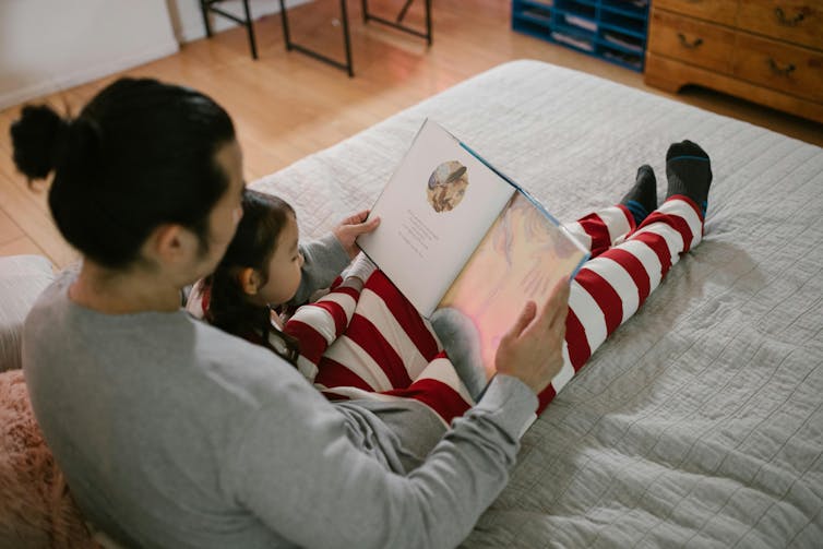 A man reads a book to a child in bed.