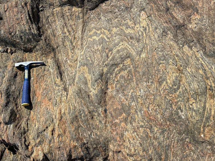 Close-up of a brown-orange rock face with wavy fold lines in it.