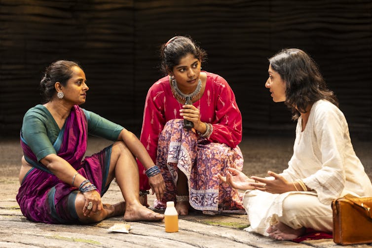 Two women in sarees talk to a woman in a churidar.