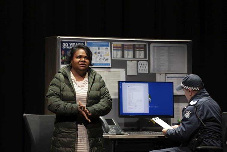 Production image: Yovich talks to a cop in a police station.