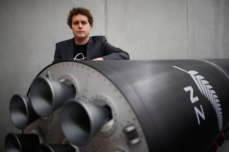 Peter Beck standing behind a large rocket painted in black with a fern.