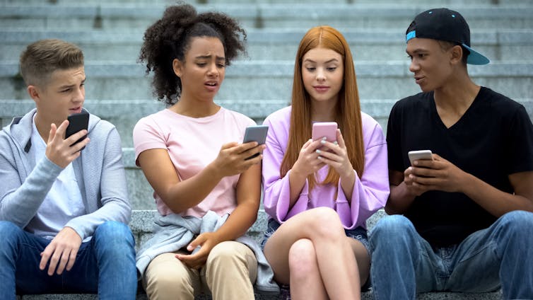 a row of people holding cellphones sit besides each other