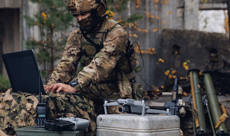 A soldier in fatigues and a face mask working at a lap top