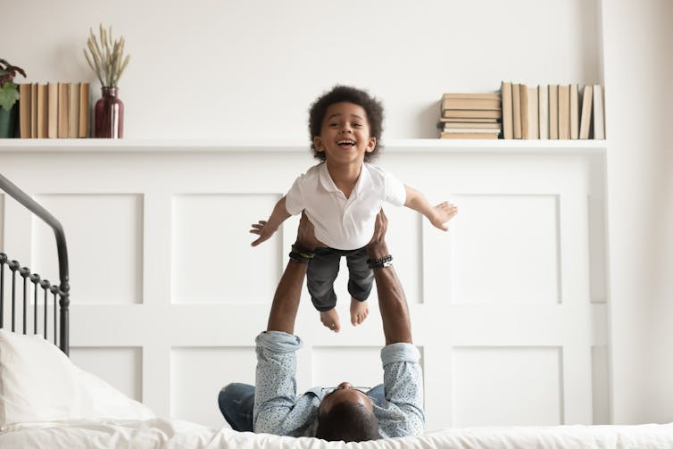 A man lying on a bed lifting a toddler above his chest